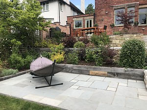 small stone patio with hammock and railway sleeper walling for flower beds