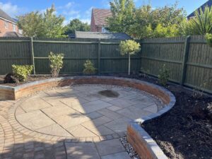 Professional landscaping of a circular sandstone patio with a curved brick garden wall in Nottinghamshire.
