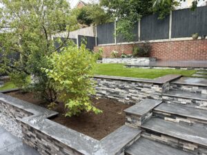 Tiered garden renovation with stacked stone garden walls, steps, and a new lawn expertly built by landscaping professionals.