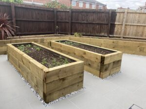 Modern garden landscaping with new raised sleeper beds and light grey porcelain patio tiles.