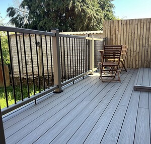 Contemporary grey composite decking area featuring a modern post and rail balustrade system with a small outdoor bistro set