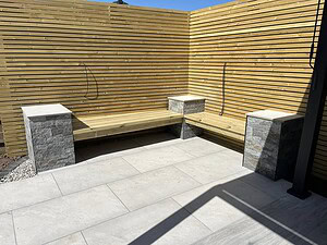 Handcrafted horizontal slatted timber privacy screen with an integrated floating corner wooden bench supported by natural Pavestone Cubo stone pillars